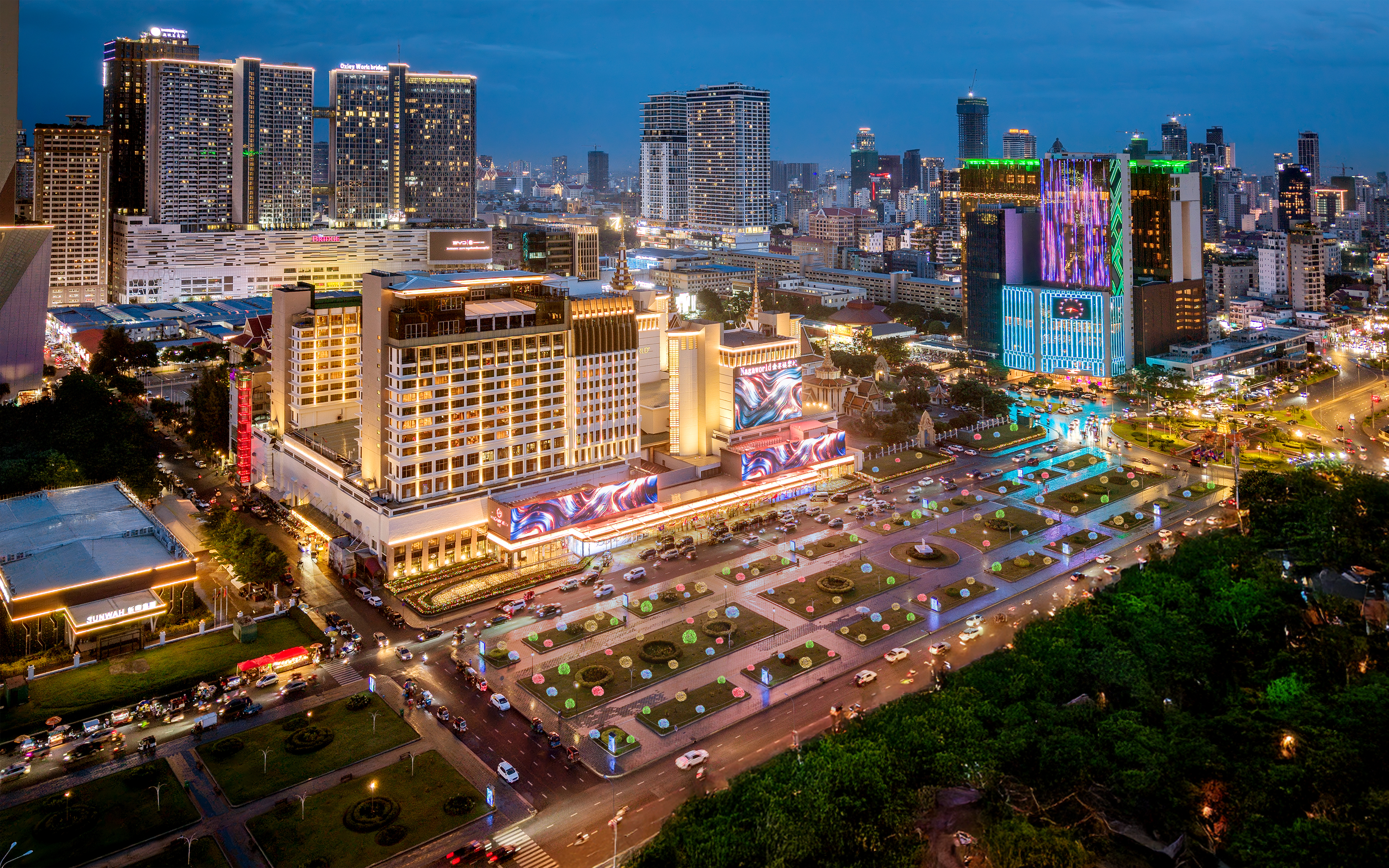 Illuminated city skyline at night with modern skyscrapers and a brightly lit plaza.