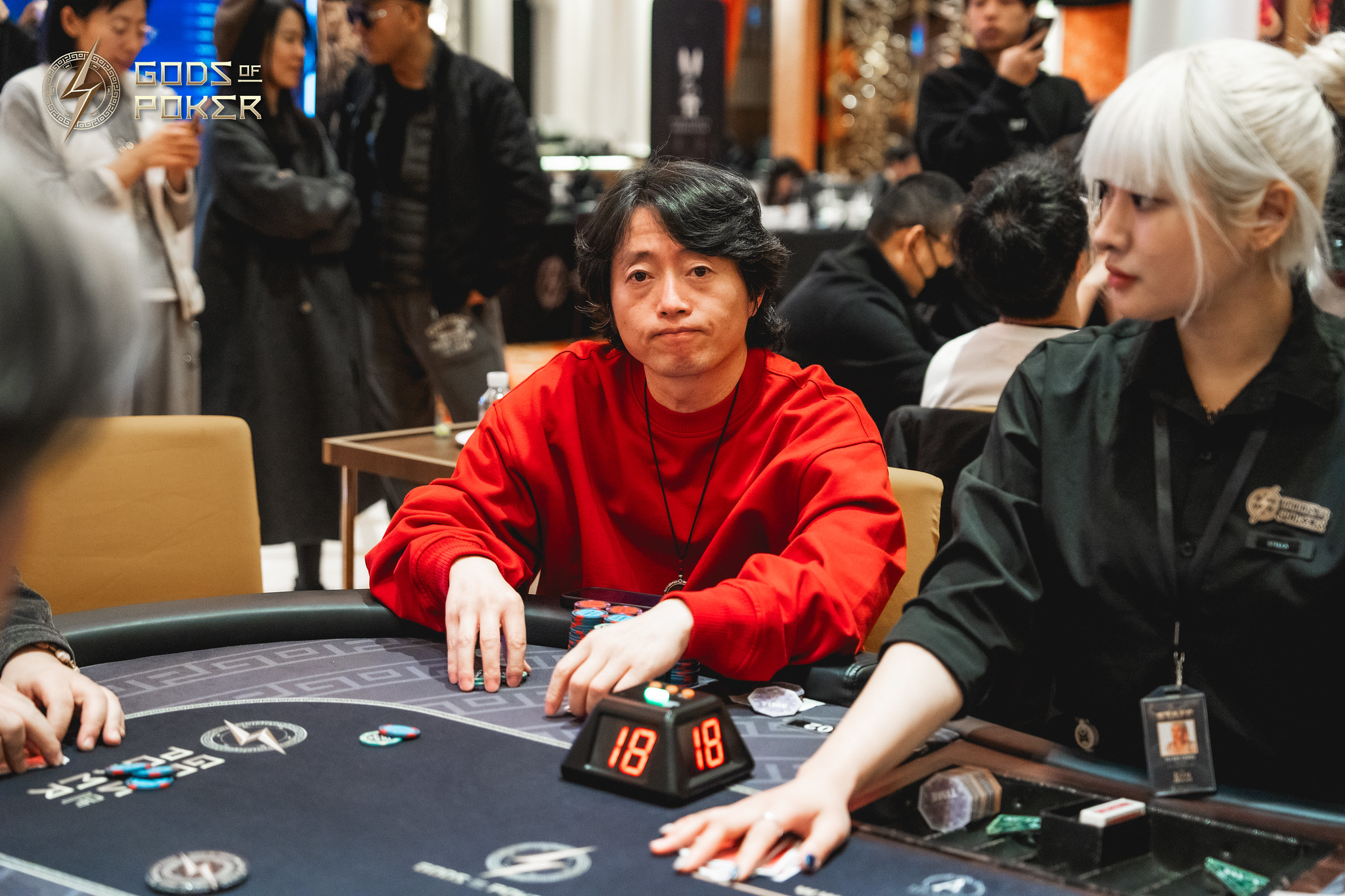 A man in a red sweater sits at a poker table with a blonde woman.