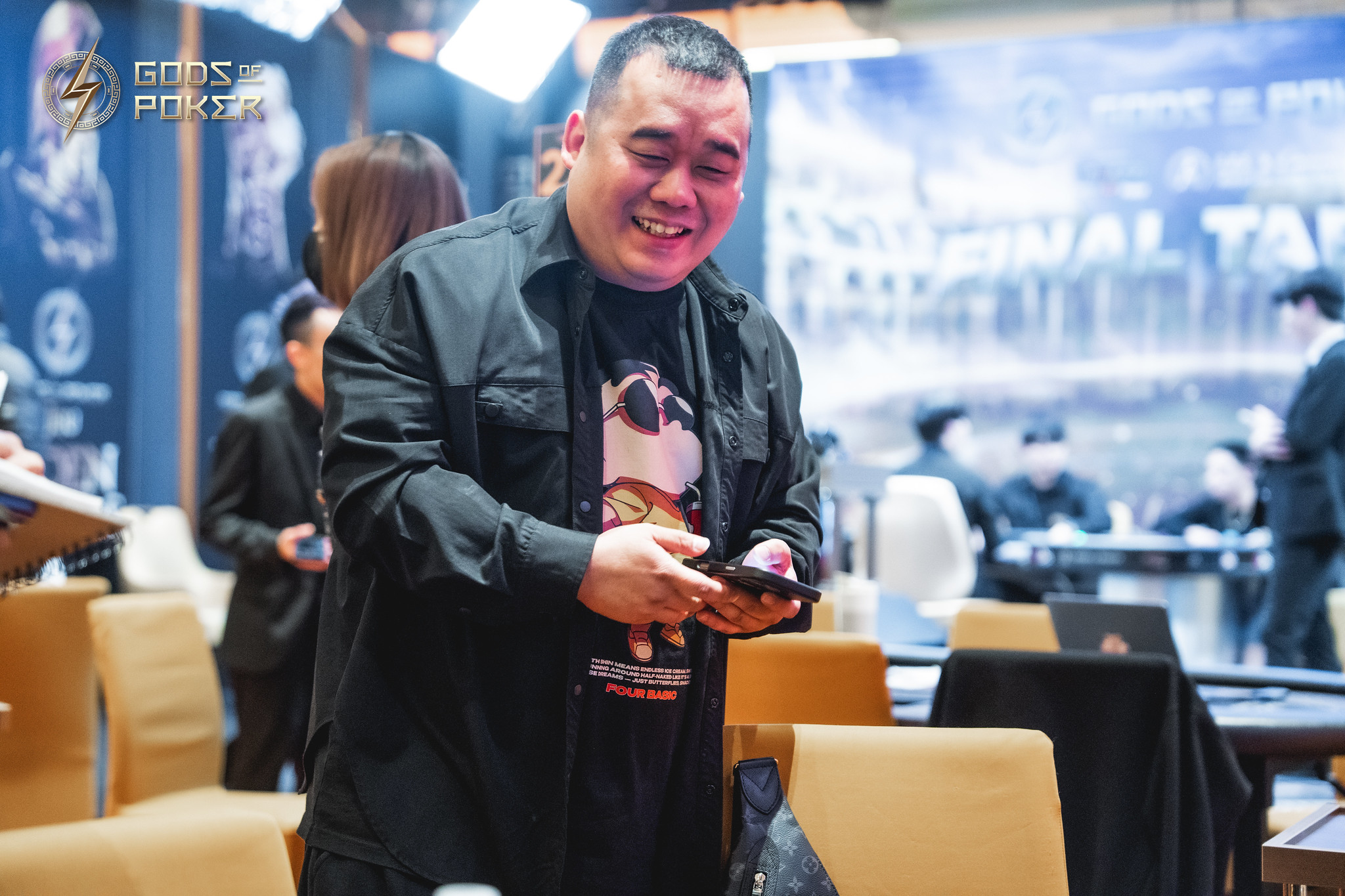 Smiling man in a black shirt holds a phone at a poker event.