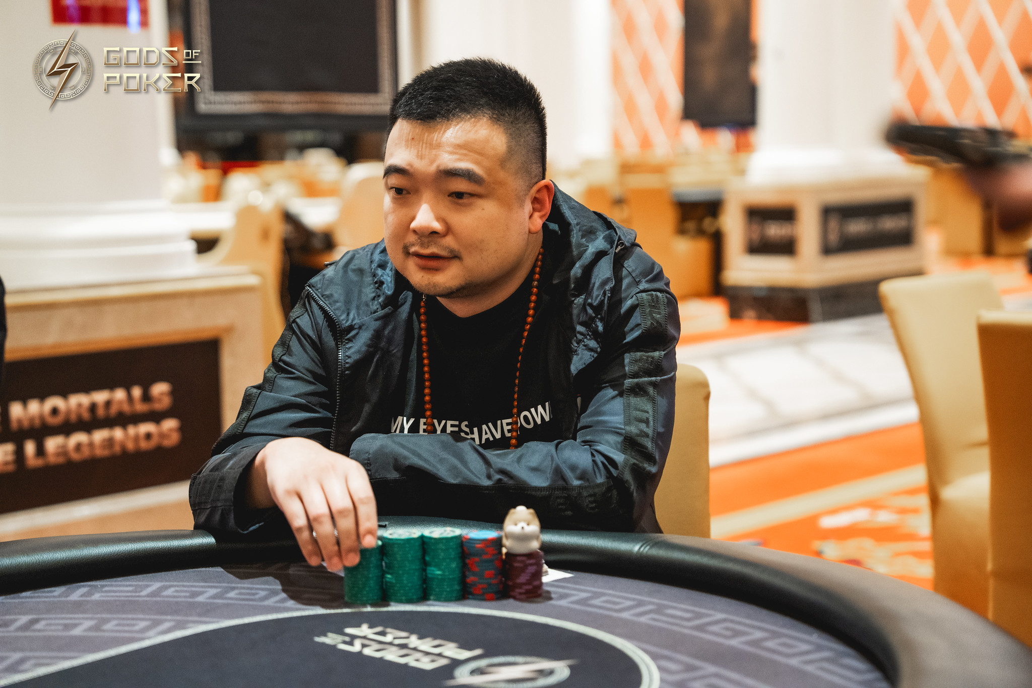 An Asian man sits at a poker table with chips, intently focused on the game.