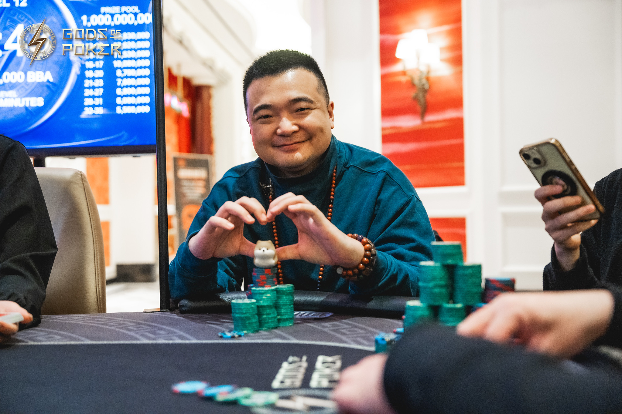Smiling man holds poker chips at a table, surrounded by stacks of green chips.