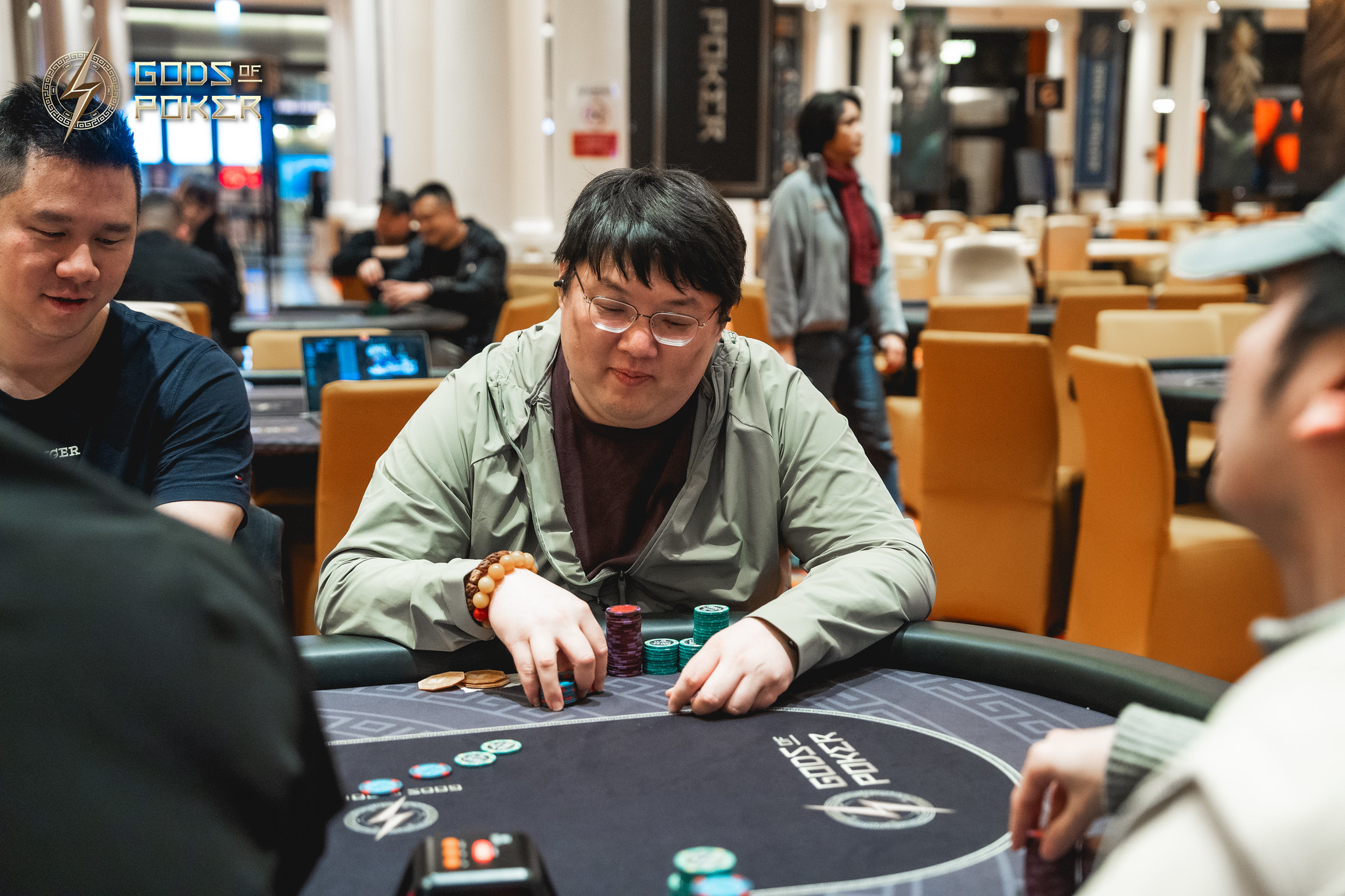 A man wearing a green jacket intently playing poker at a casino table with chips.