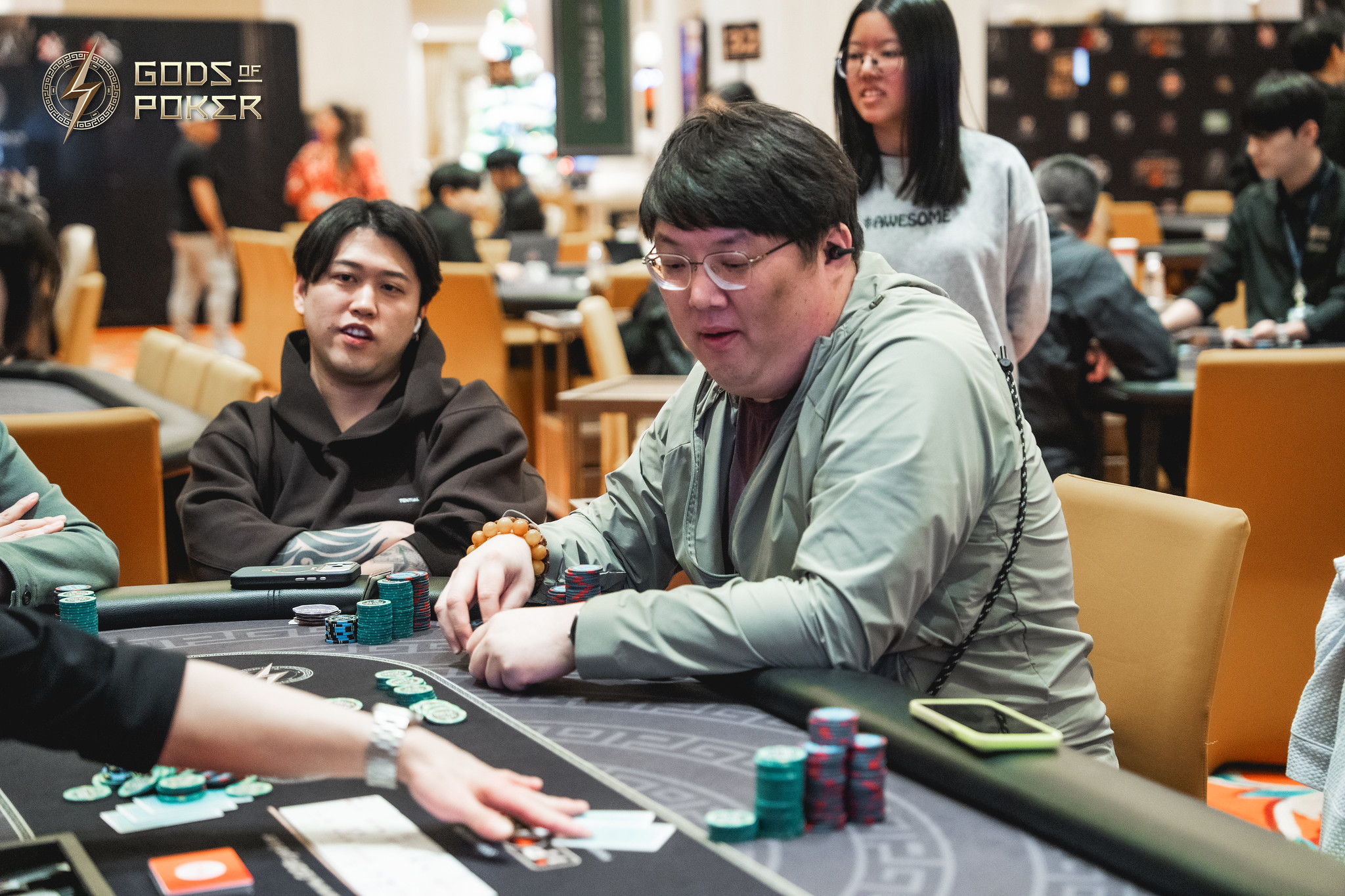 A man in a green shirt plays poker, intently looking at his cards at a casino table.