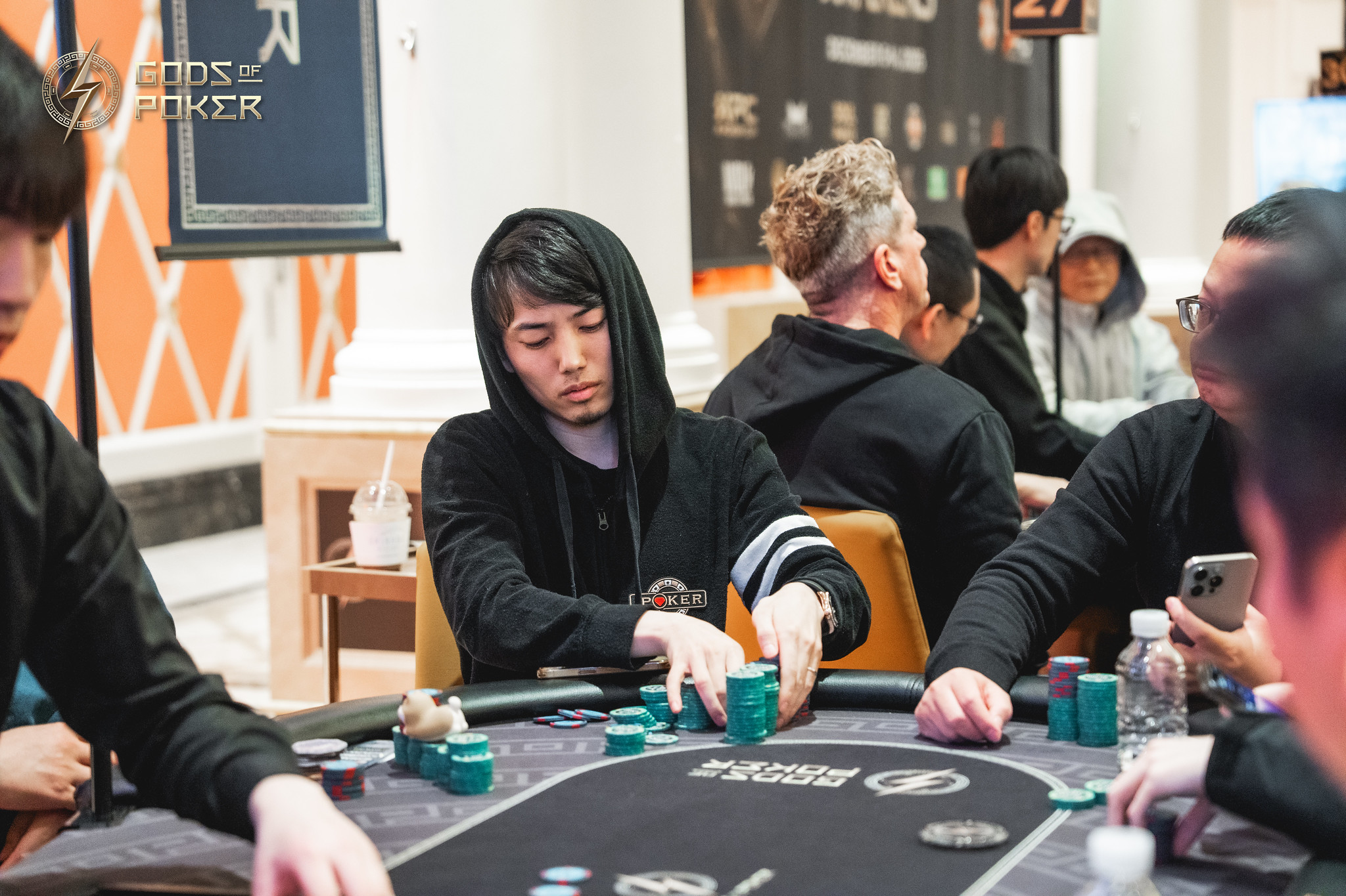 A poker player in a black hoodie intently plays cards at a casino table with chips.
