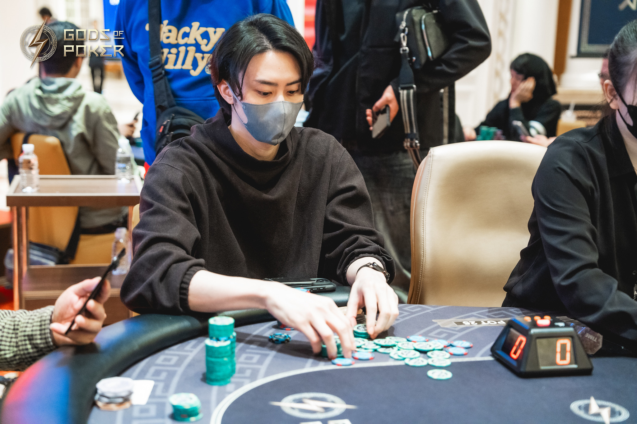 Young man in a gray mask playing poker, moving green chips on a felt table.