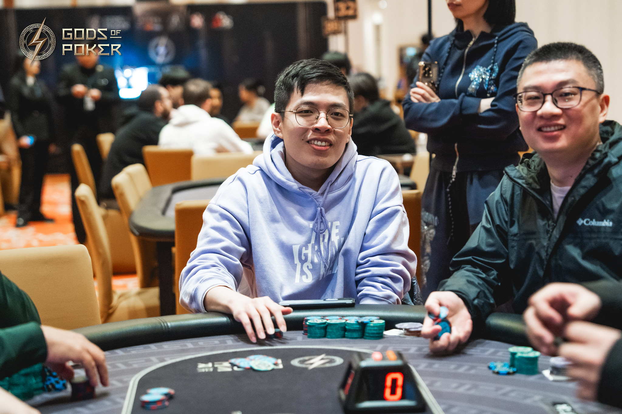 Two men smile, playing poker at a casino table with chips.