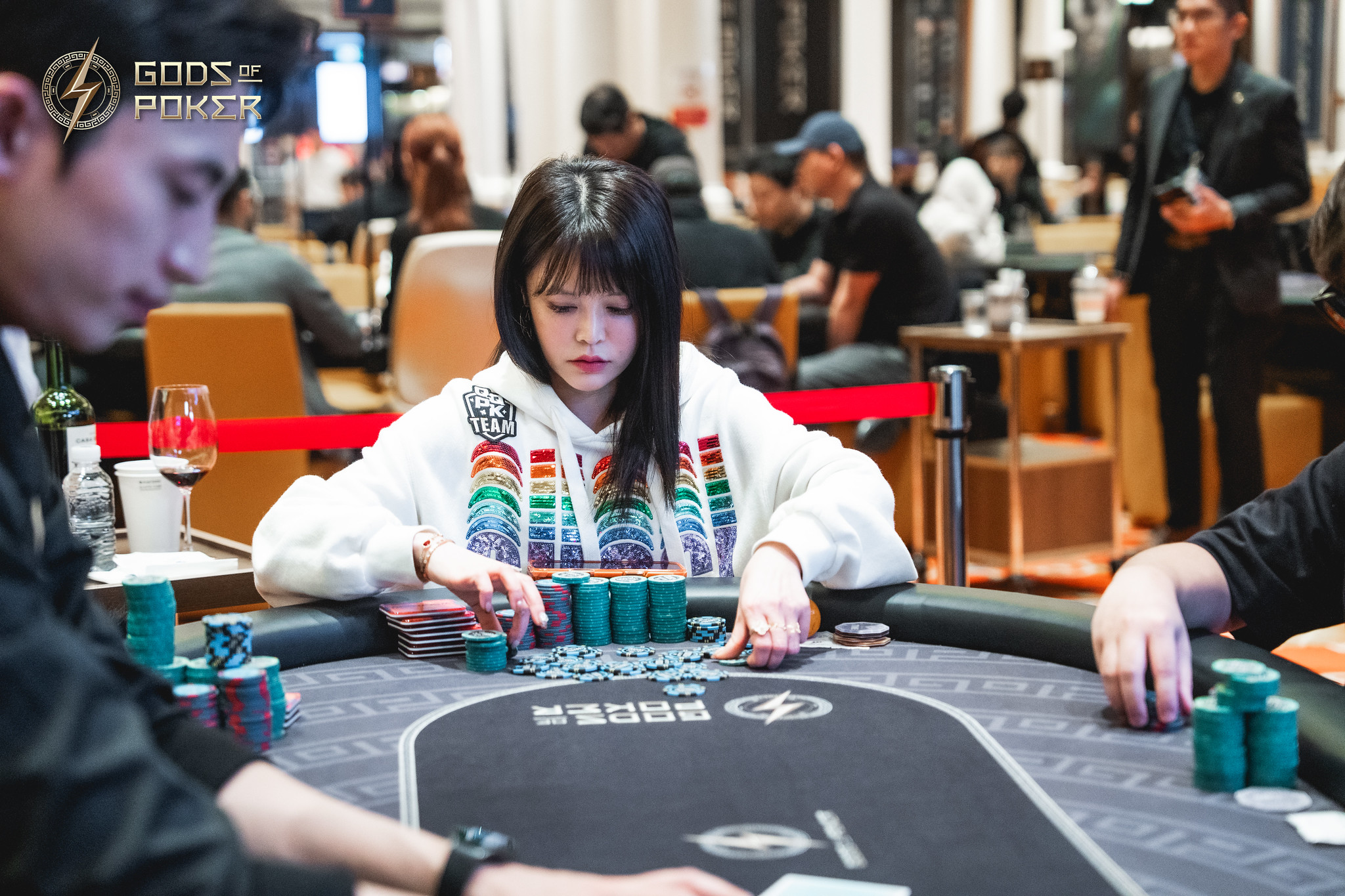 Woman in a rainbow hoodie playing poker, meticulously arranging her chips at a casino table.