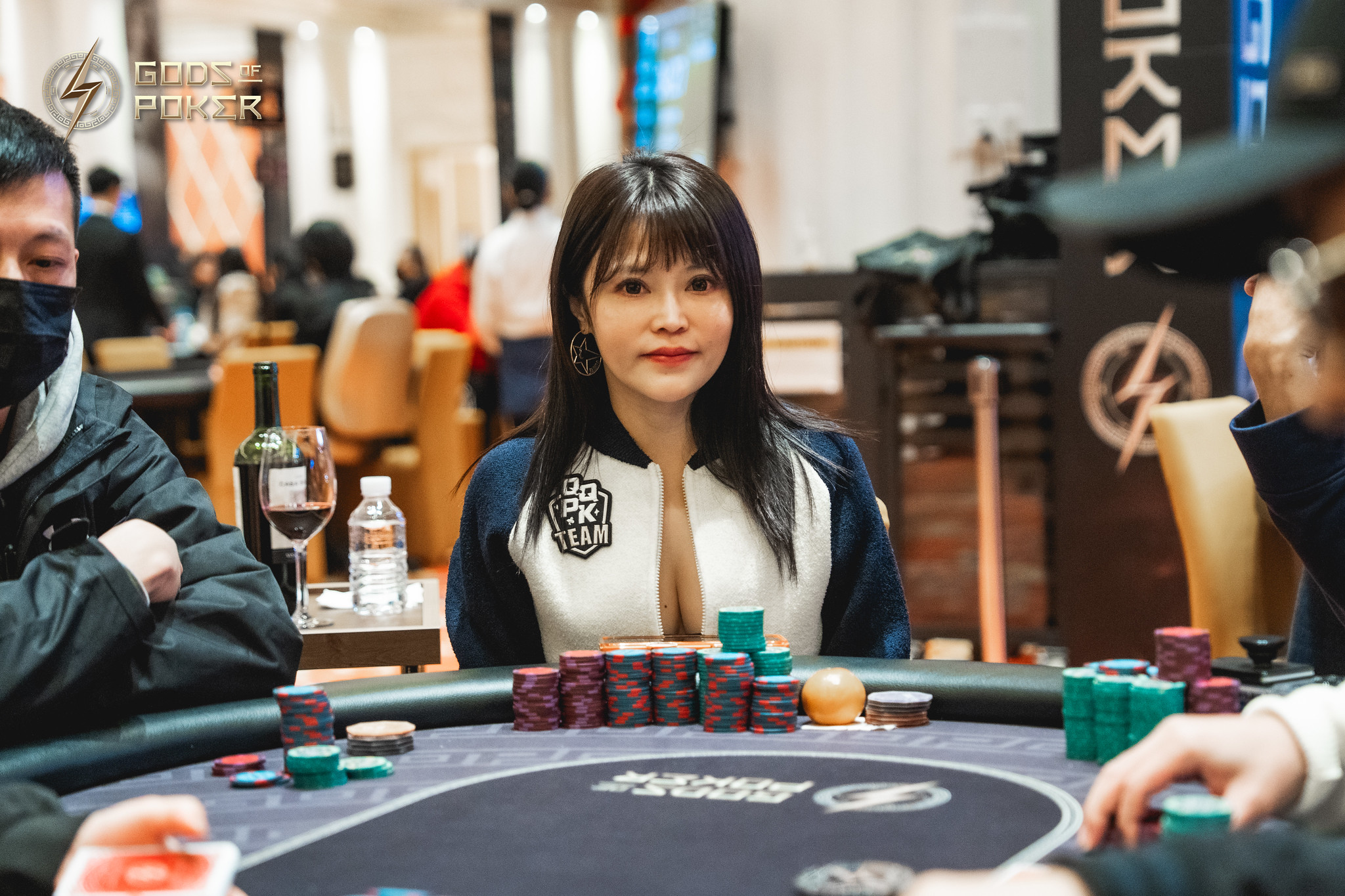 A woman with dark hair and a jacket sits at a poker table with chips.