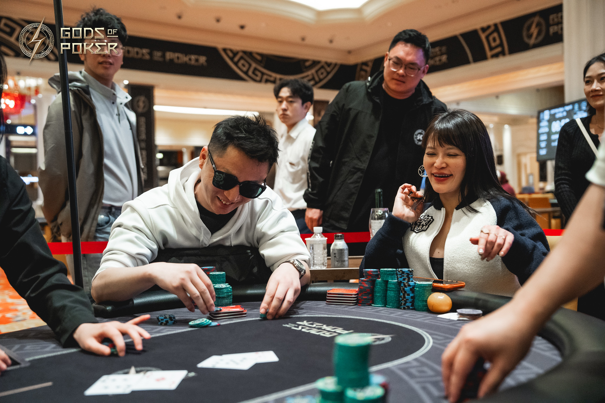 Man in sunglasses and woman with chips playing poker at a casino table.