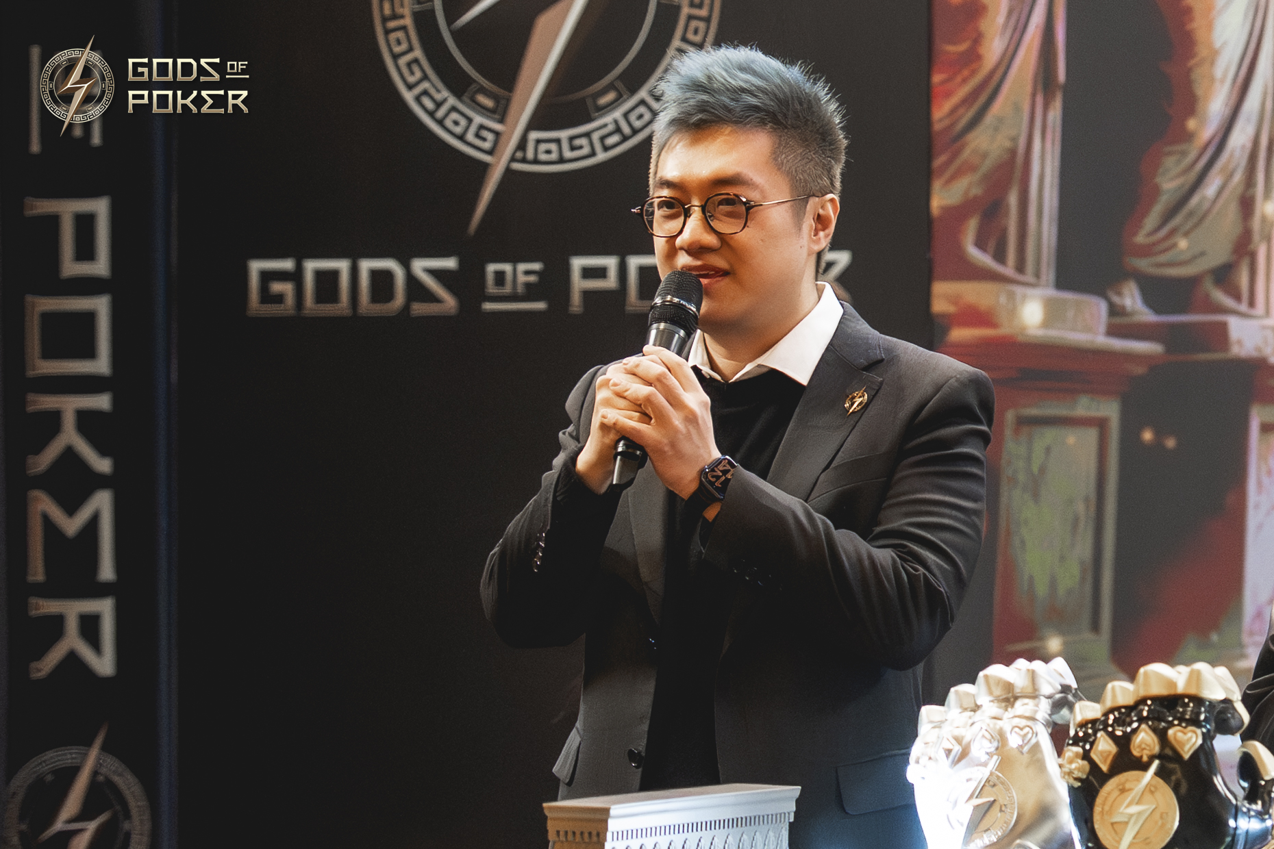 A man in glasses speaks into a microphone at a