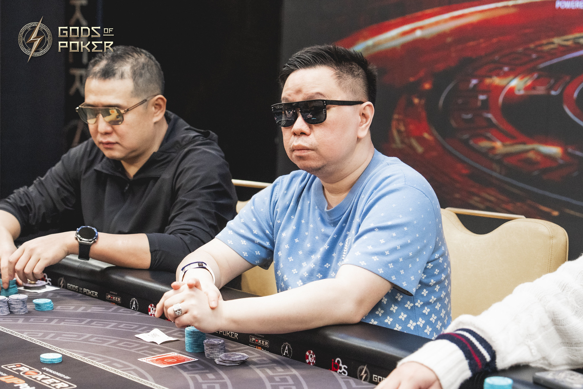 Two men playing poker at a table, one in sunglasses, both focused on the game.