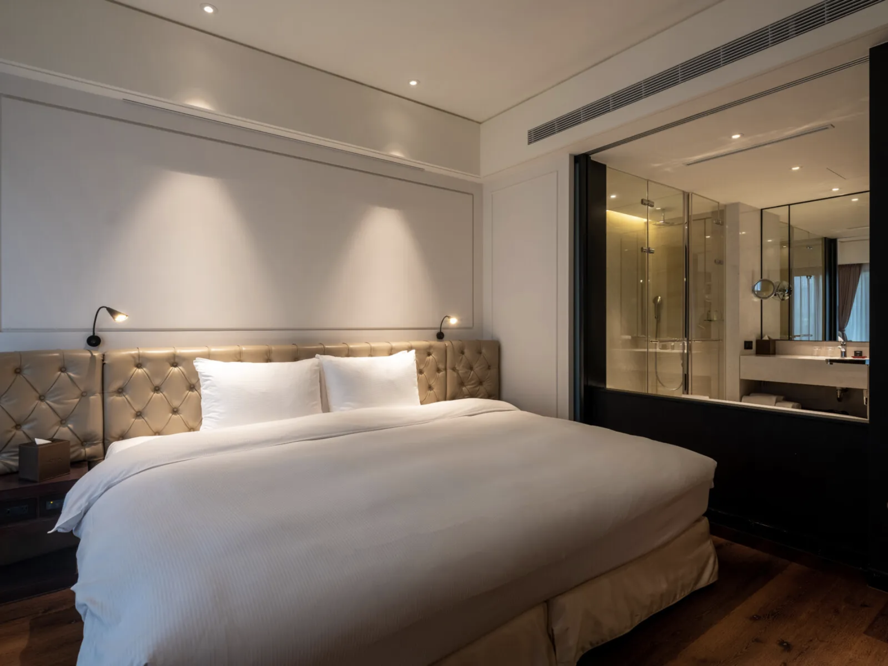 Modern hotel bedroom featuring a large bed and an en-suite glass-partitioned bathroom.