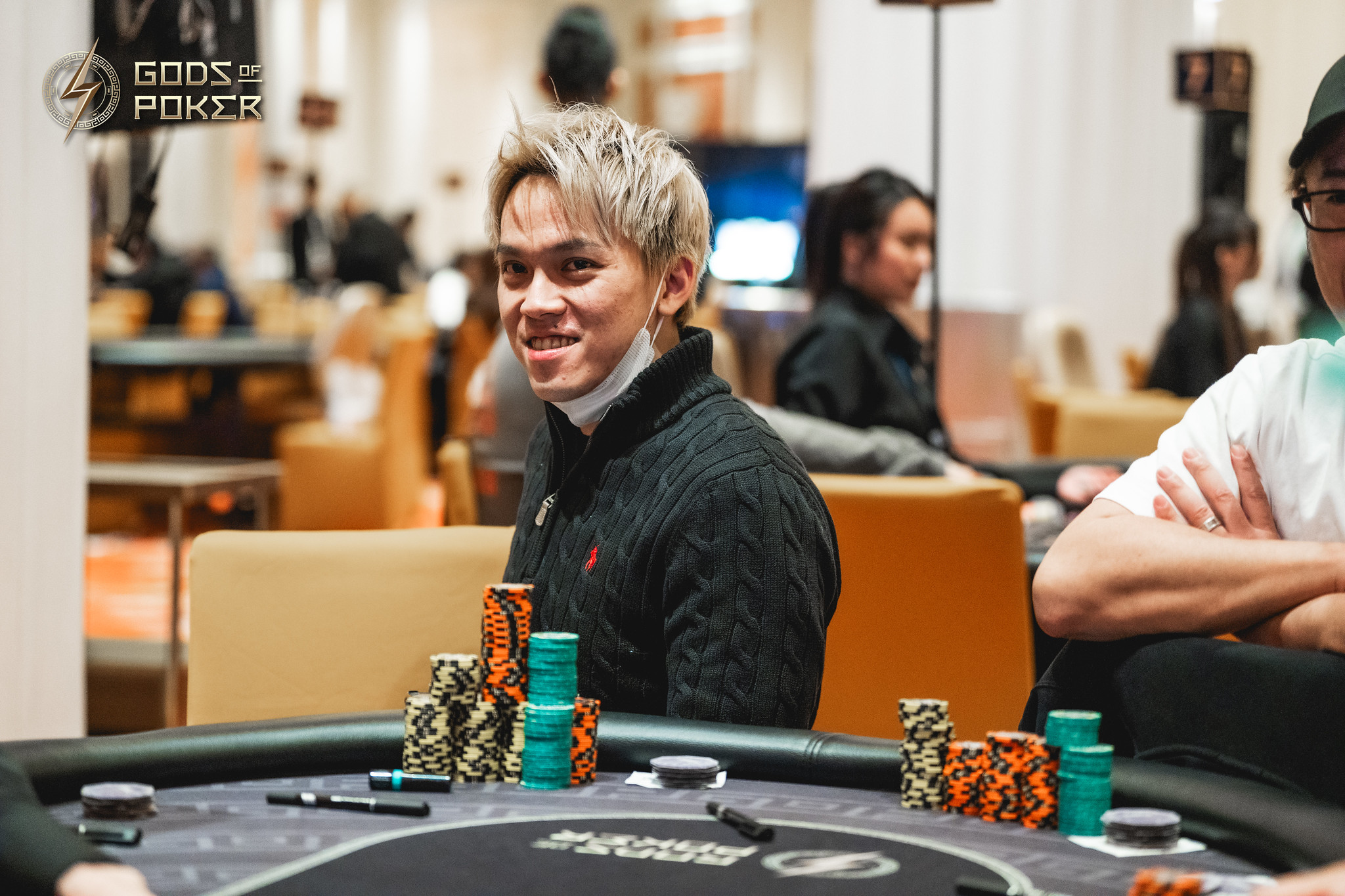 Smiling man with light hair sitting at a poker table with stacks of chips.