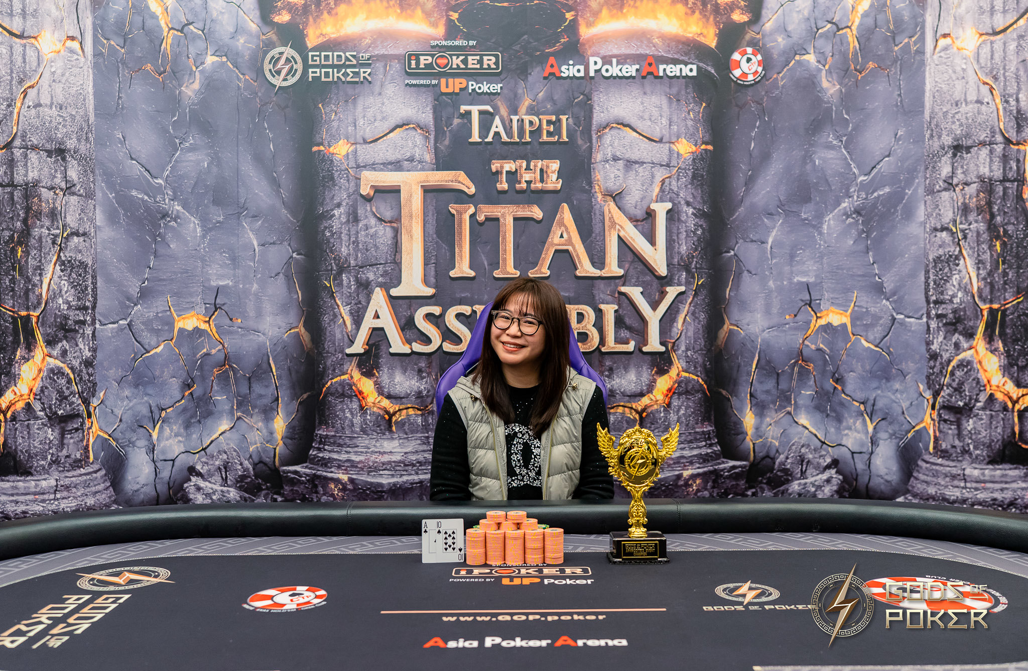 Smiling woman with poker chips and a gold trophy at 'Taipei The Titan Assembly'.