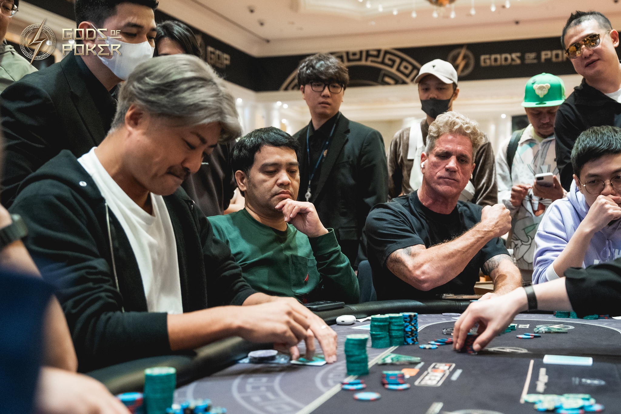Men intently playing poker at a casino table with chips and onlookers.