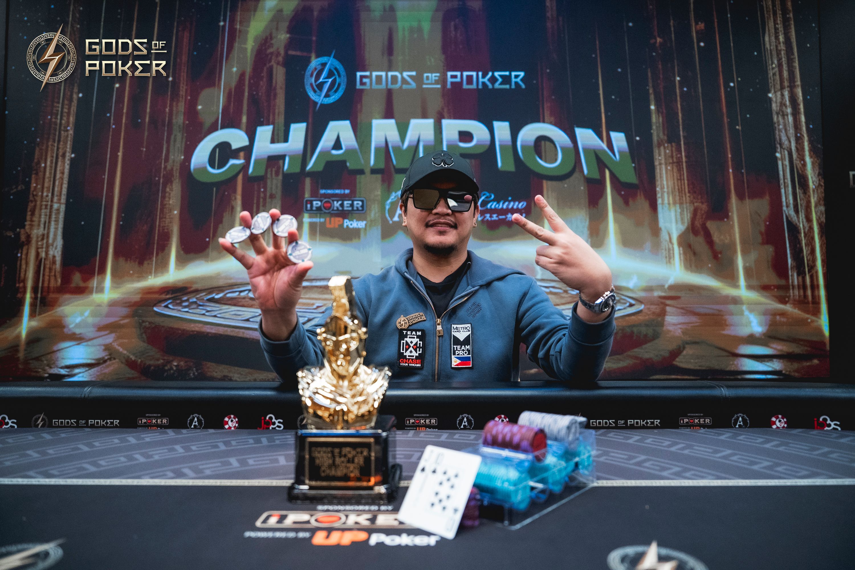 A poker champion celebrates his victory with a golden trophy and chips, making a peace sign.