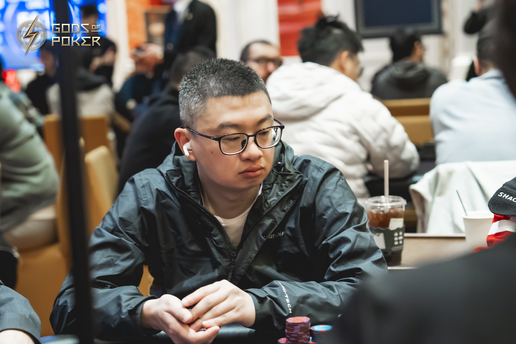 Man in glasses intently watches a poker game at a casino table.