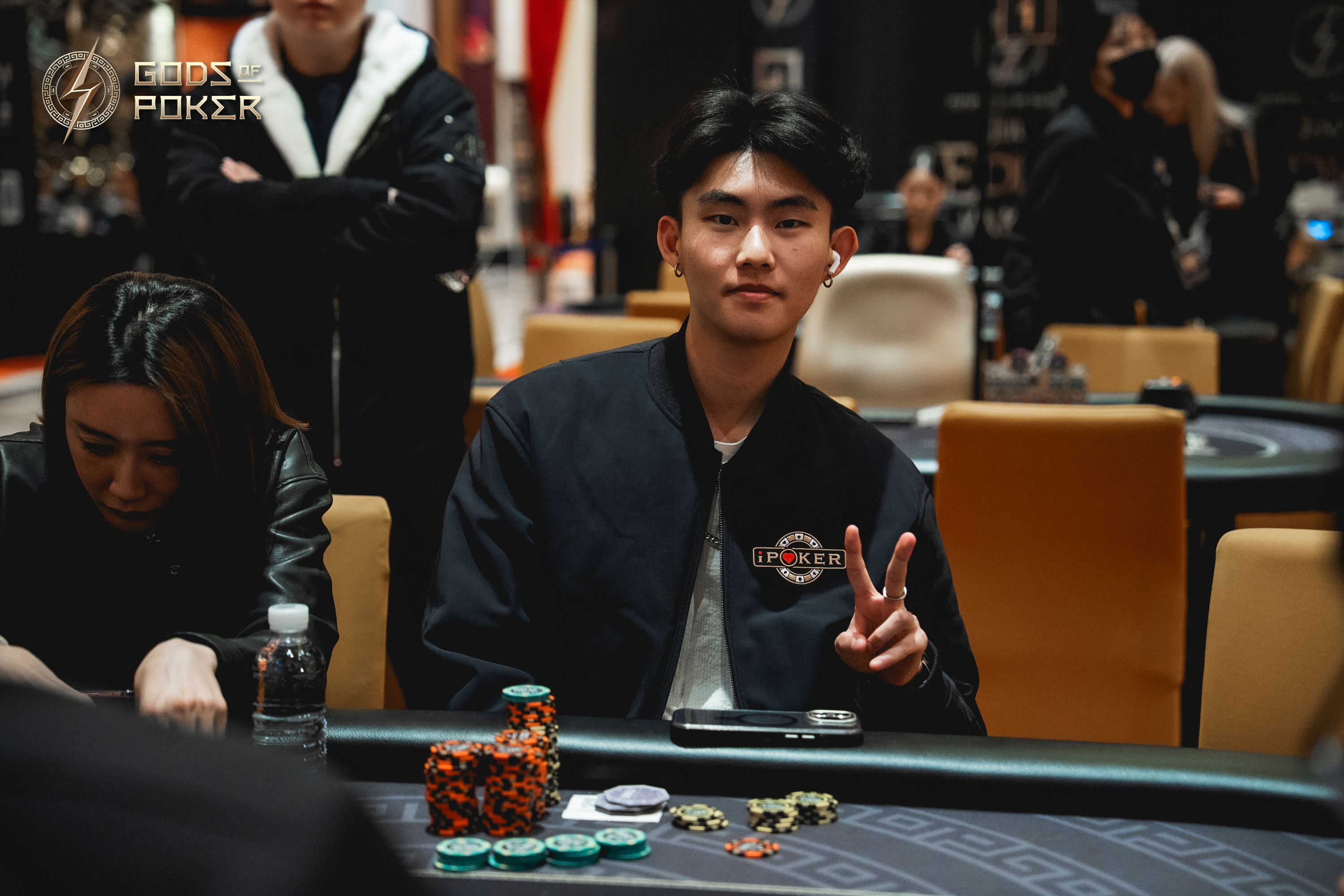 Young man at a poker table flashes a peace sign amidst poker chips and cards.