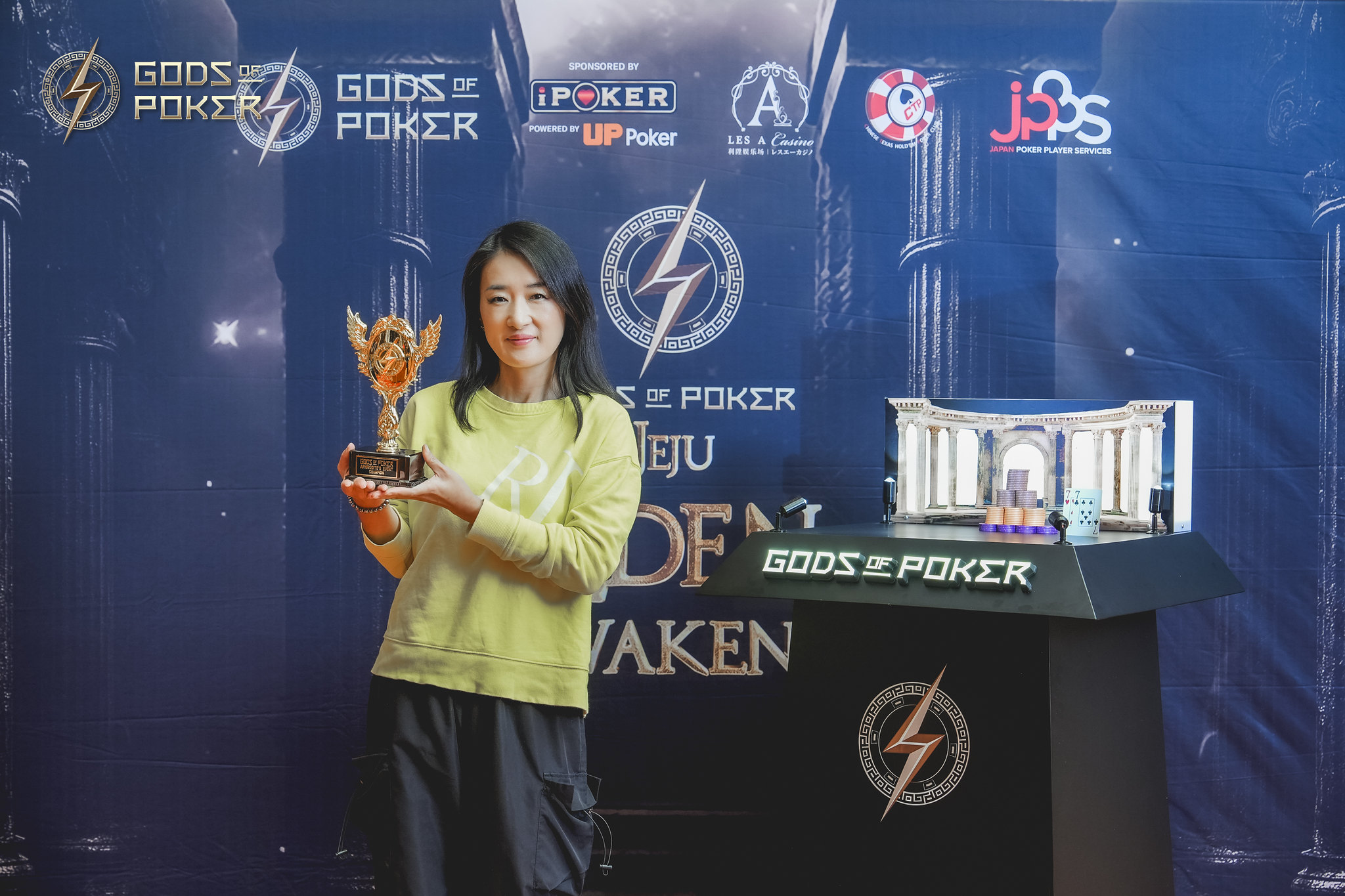 Smiling woman proudly holds a golden trophy at a Gods of Poker event.