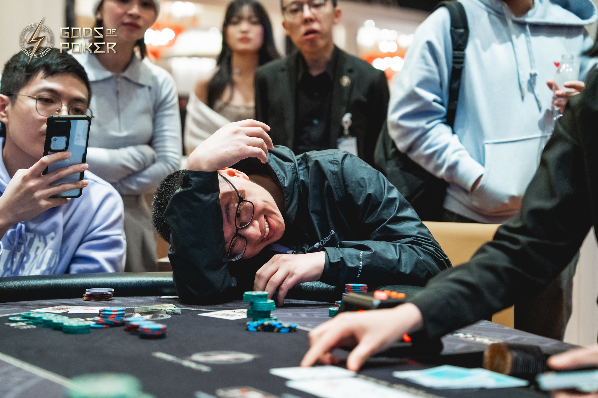Man slumped over a poker table, looking dejected during a game, with observers in the background.