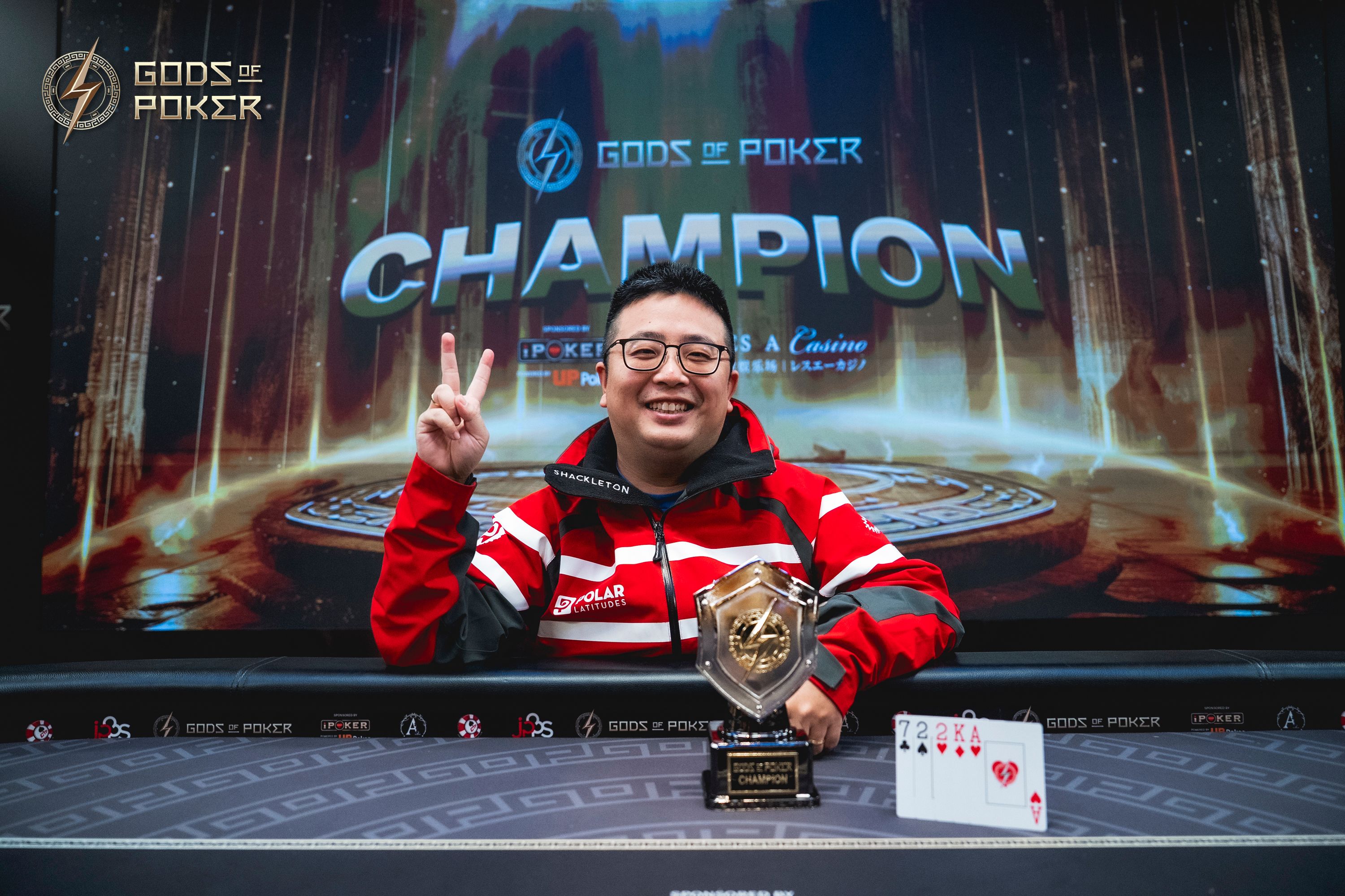Smiling champion makes a V-sign, holding a poker trophy with a royal flush hand.