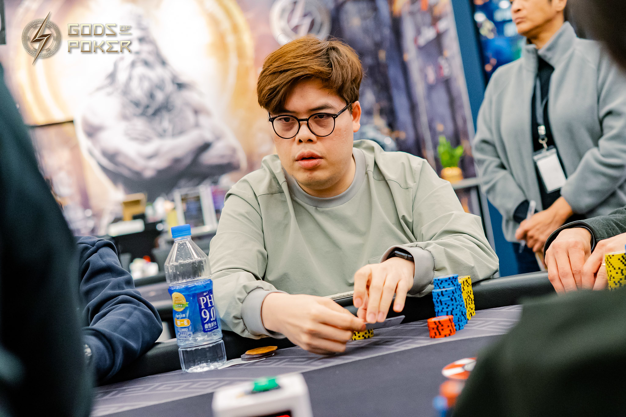 Man in glasses intently plays poker, handling chips at a tournament table.
