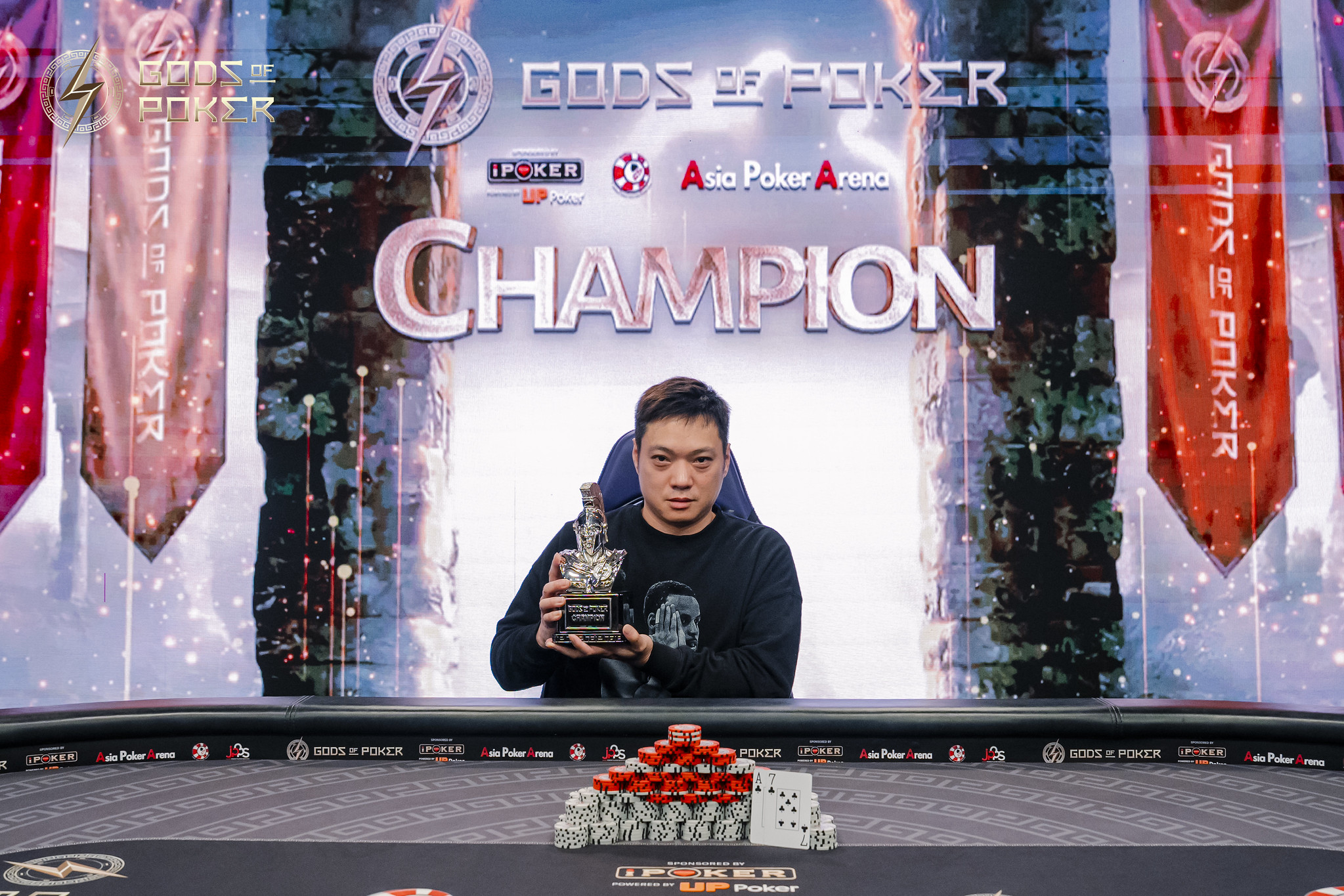Poker champion holding a trophy in front of a 'GODS OF POKER CHAMPION' screen.