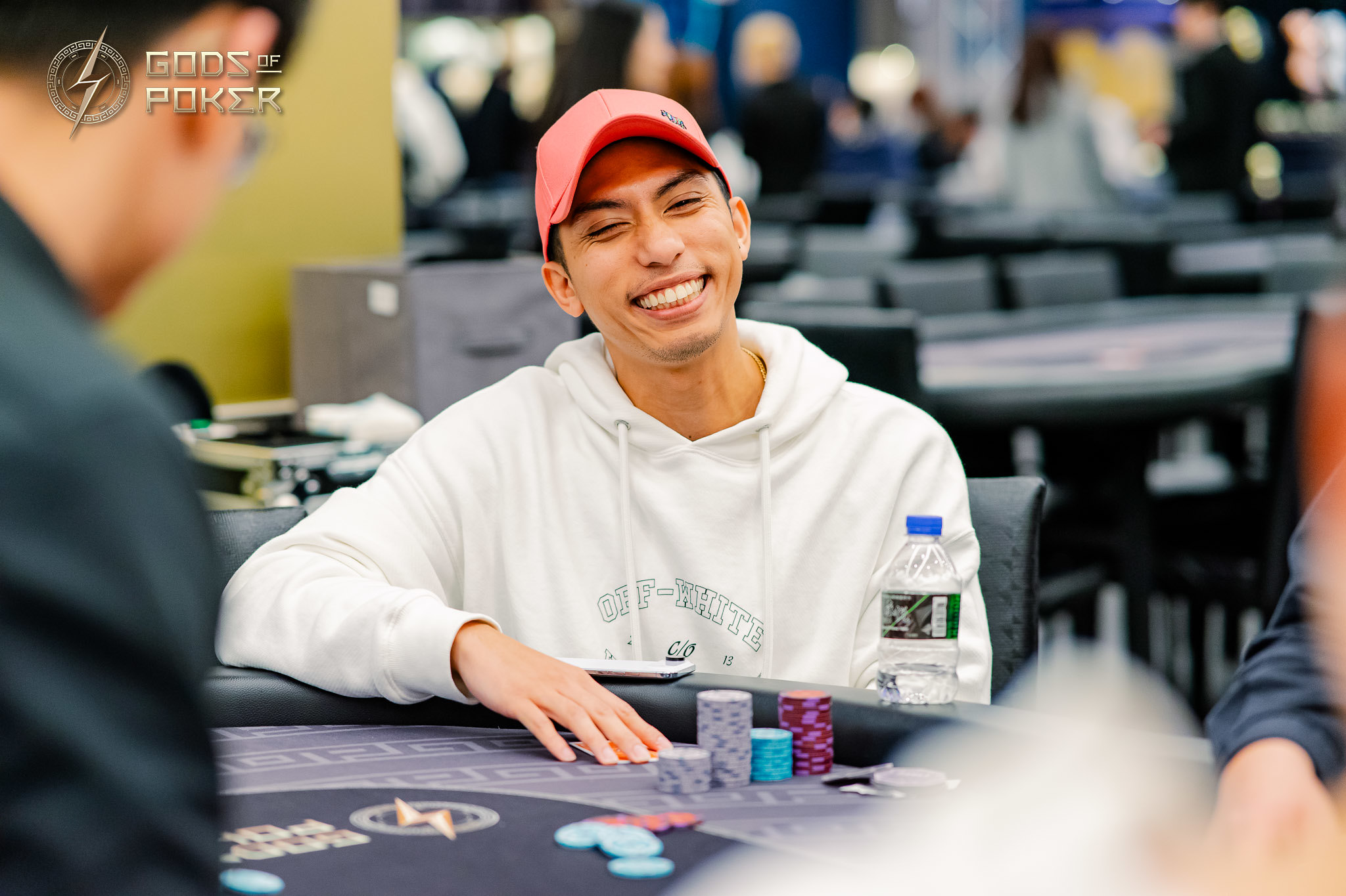 Smiling man in a white hoodie and red cap at a poker table with chips.