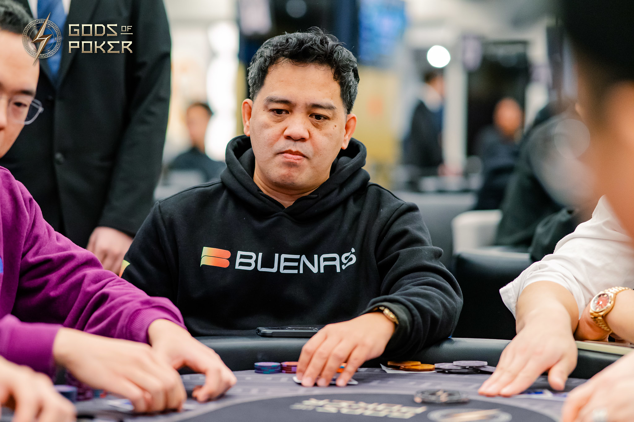 Man in a black hoodie with 'BUENA$' sits intensely at a poker table.