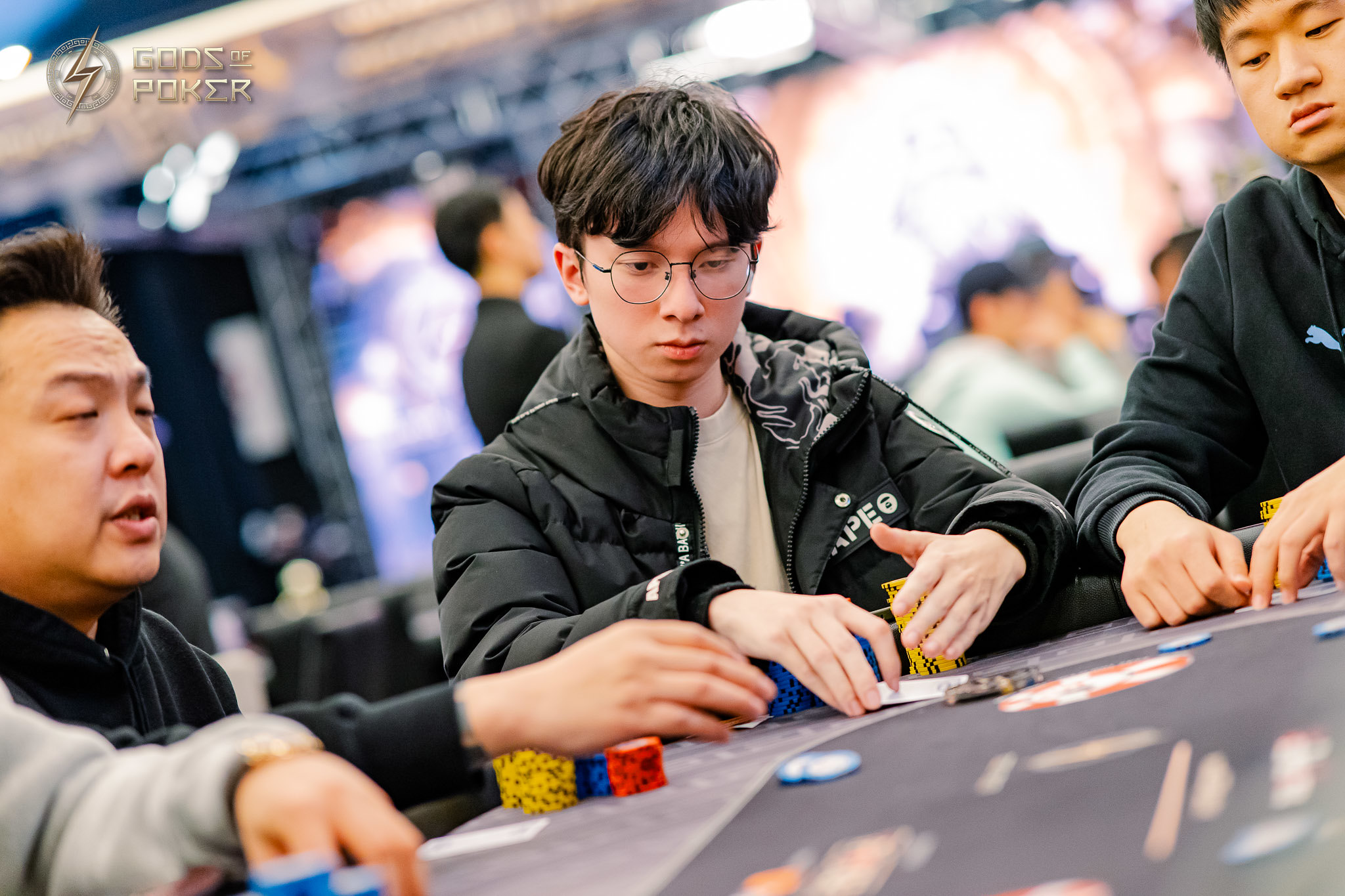Young man in glasses intently plays poker, focusing on his chips and cards.