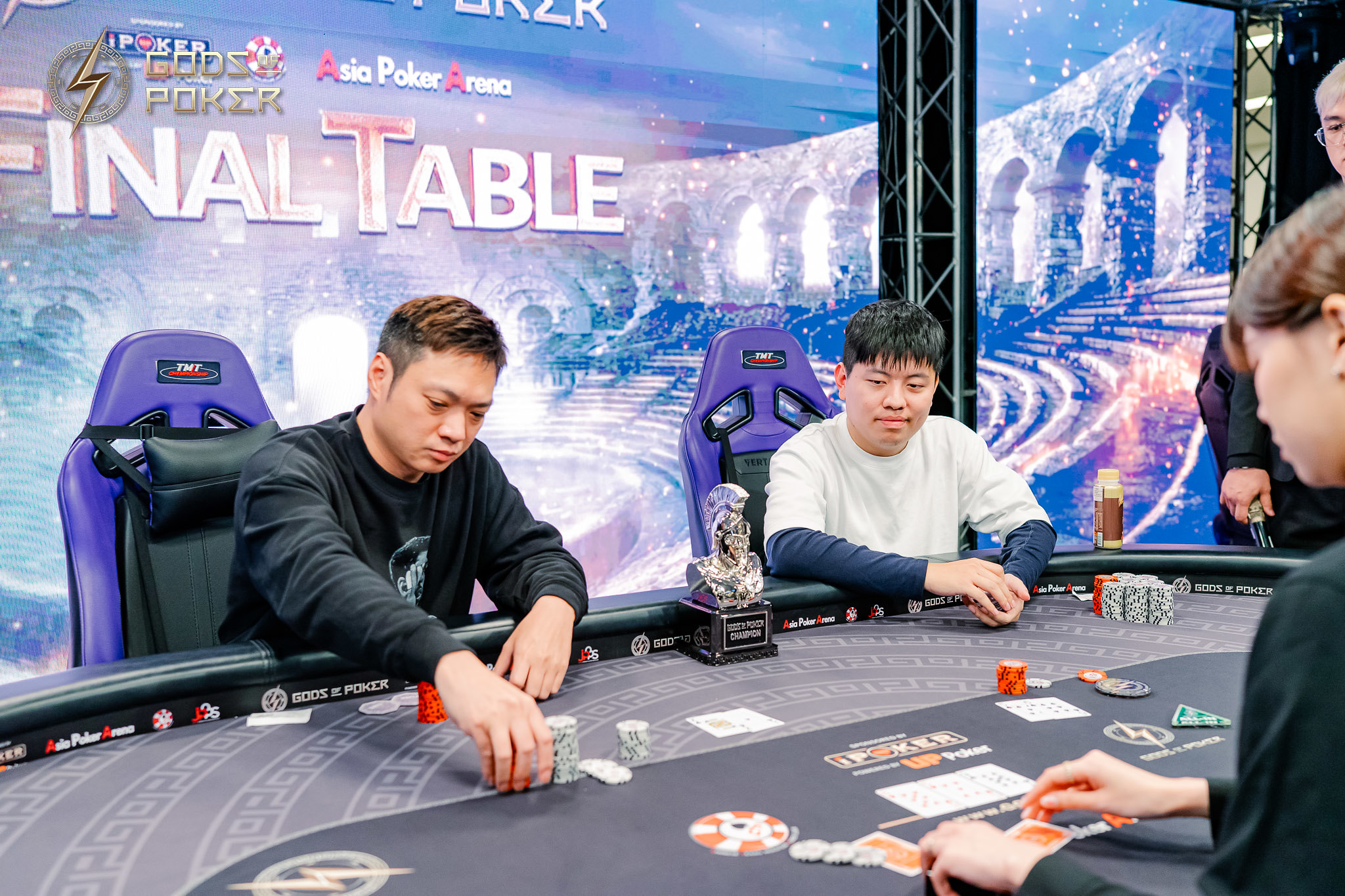 Two men play poker at a final table, surrounded by chips and cards.