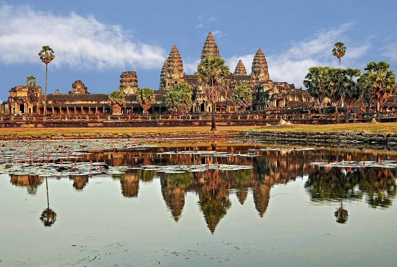 Angkor Wat temple complex reflected in a calm lake under a blue sky.