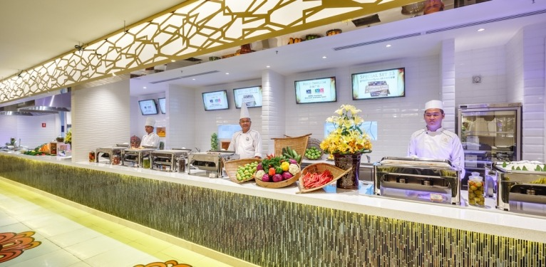 Chefs stand behind a vibrant buffet counter filled with fresh produce and hot dishes.