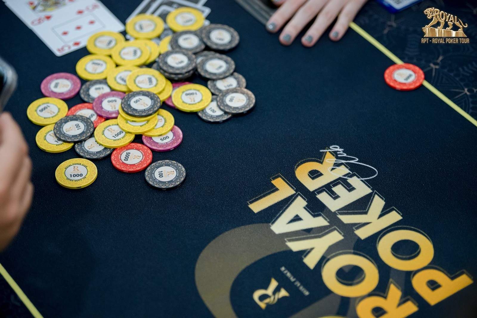 Poker chips and playing cards on a black 'Royal Poker' table during a game.