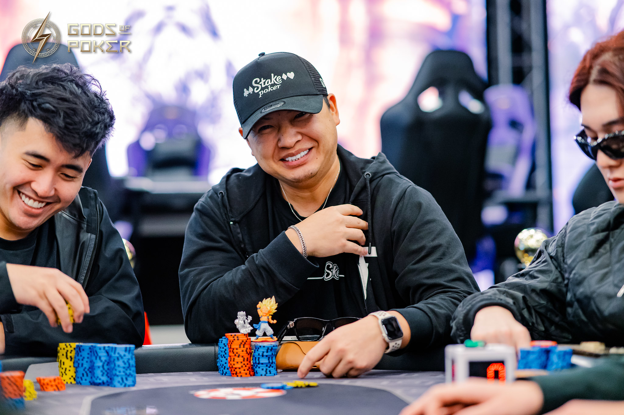 Smiling man in black cap and hoodie at a poker table with colorful chips.