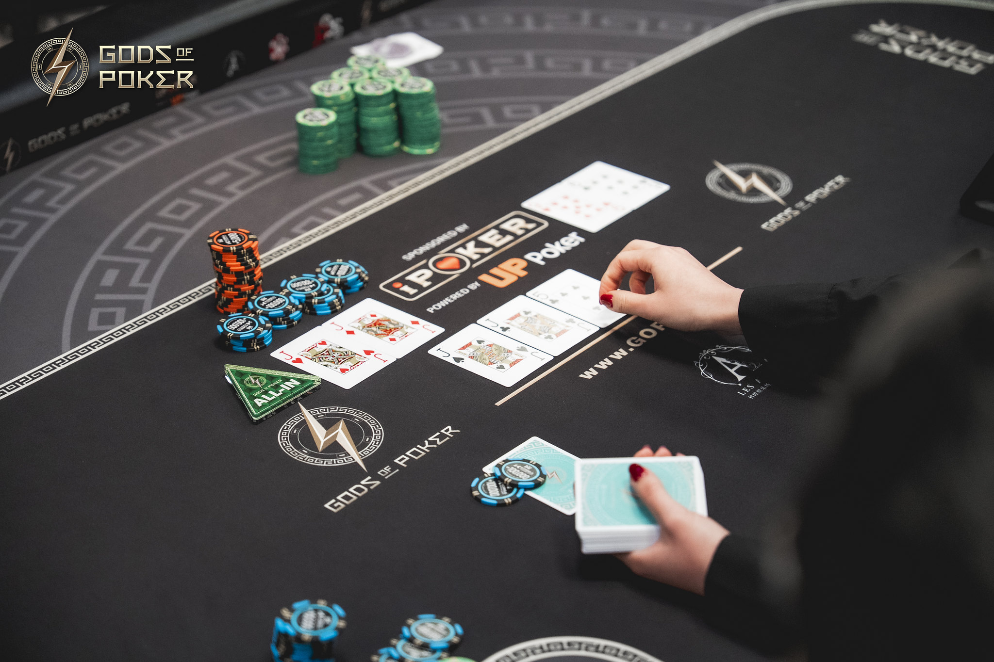 A person's hands deal cards on a branded black poker table with chips.