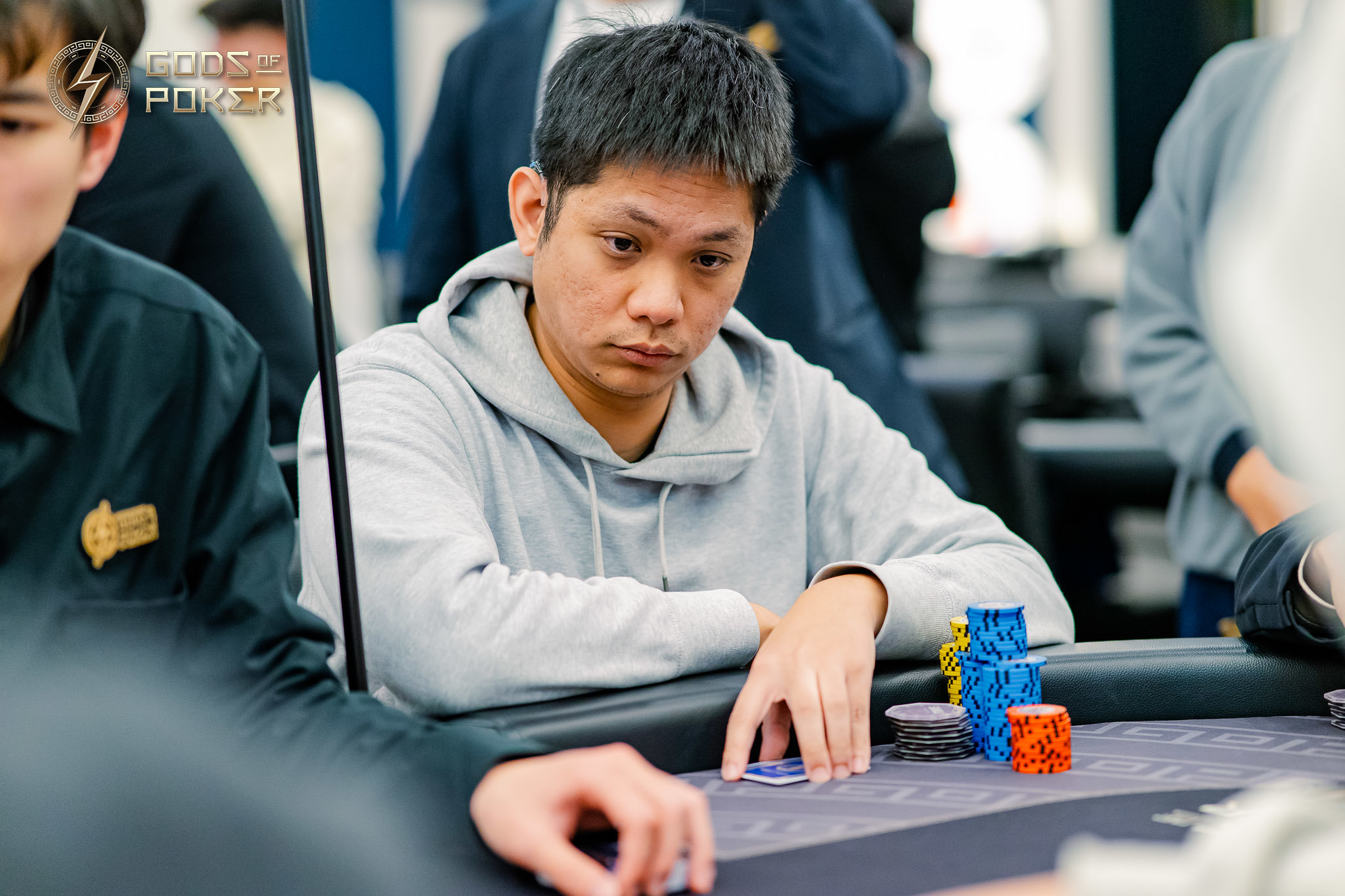 Poker player in grey hoodie focused on game at table with colorful chips.