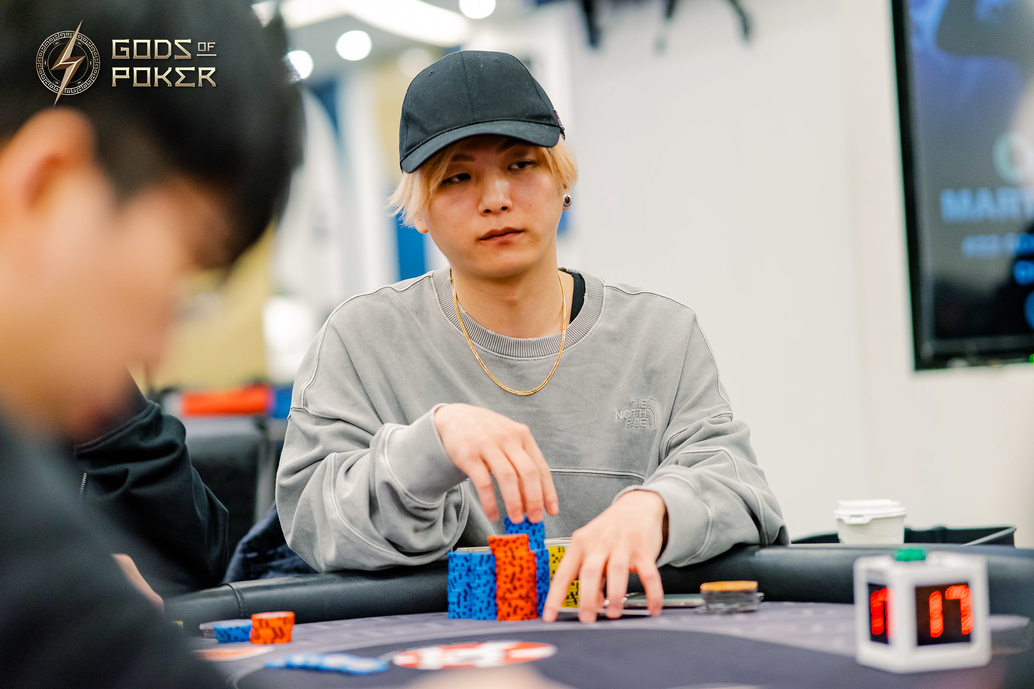 Young man in a black cap and grey sweatshirt intently playing poker, stacking colorful chips.