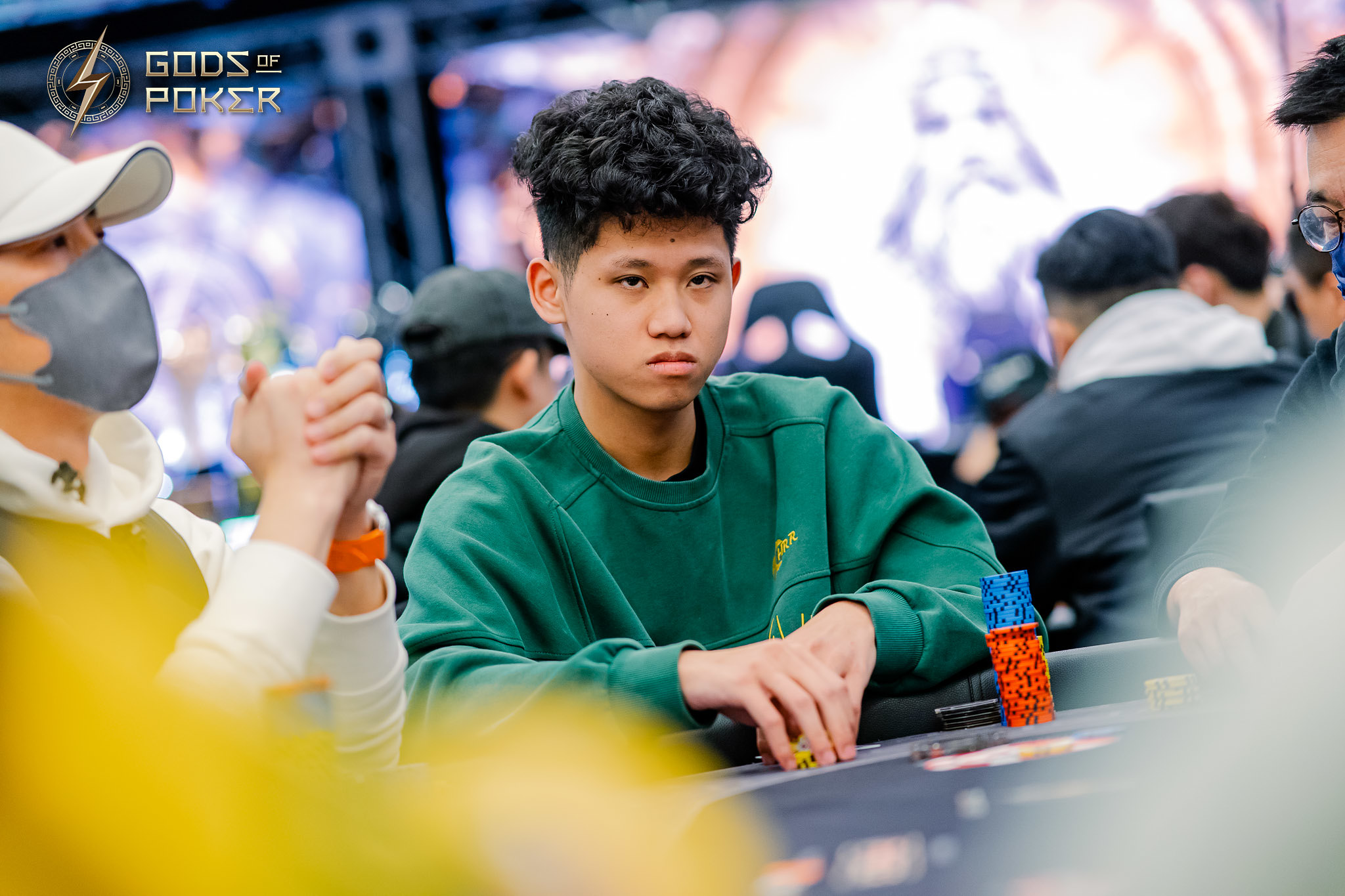 Young man in green sweatshirt intently playing poker at a casino table.