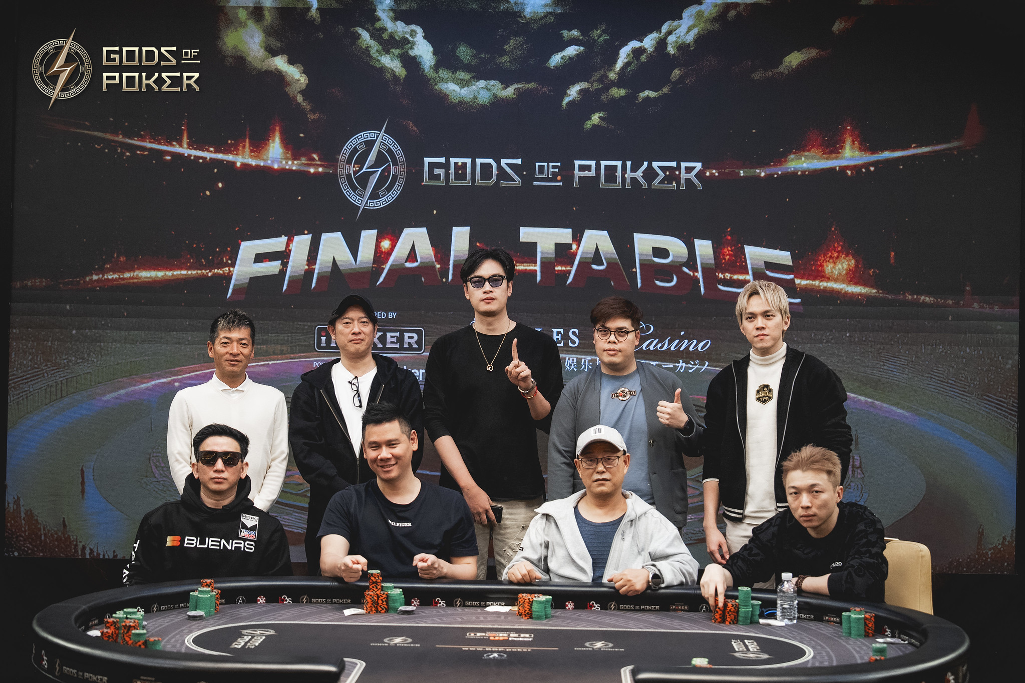 Nine poker players pose around a table at the Gods of Poker Final Table event.